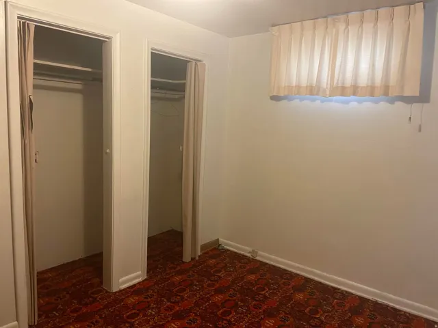 Room featuring dual closet openings with interior curtain coverings, wall-to-wall patterned carpeting, and painted baseboards