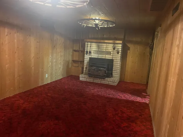 Spacious room featuring wood paneling, a brick fireplace with an insert, built-in shelving, and a wagon wheel light fixture