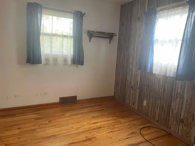 Wood-finish flooring with baseboard trim, complemented by a wood panel accent wall