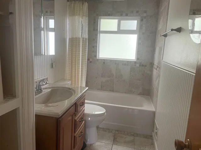 Bathroom featuring a tile-surround tub, wood-finish vanity with integrated sink, chrome faucet, and patterned floor tile