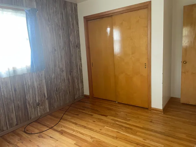 Hardwood flooring throughout featuring wood-paneled wall accents and ample closet space with sliding doors