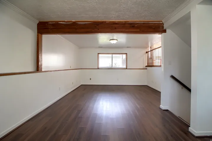 Spacious interior with wood-finish flooring, white walls, and a wood accent beam