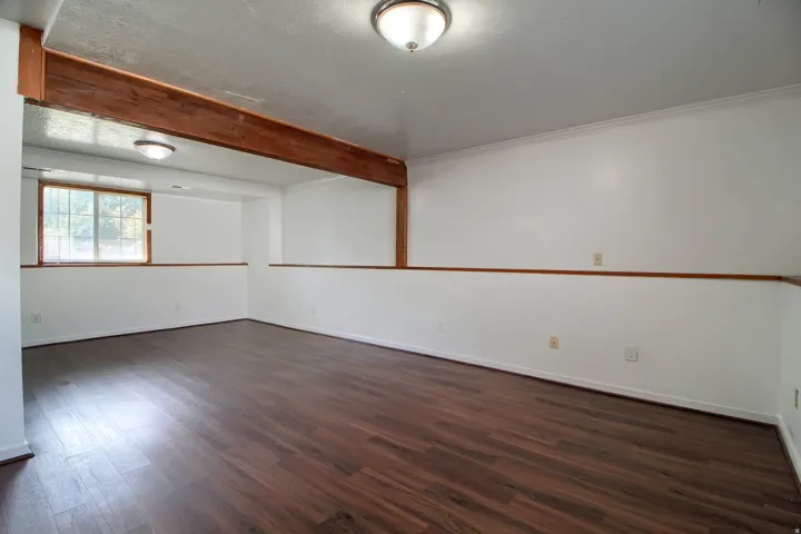 Room with wood-finish flooring, white walls, wood trim, and a window