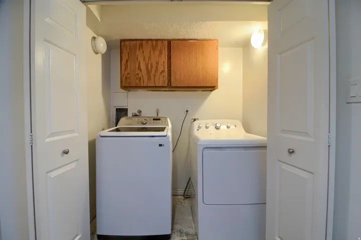 Dedicated laundry room featuring side-by-side washer and dryer appliances, wood-finish cabinetry with overhead storage, tile flooring, and recessed lighting