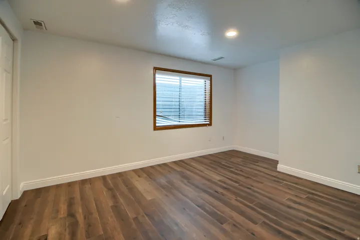 Spacious room featuring wood-finish flooring, recessed lighting, and a window with wood trim and blinds