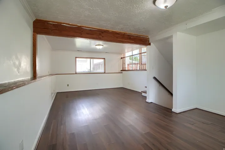 Spacious room featuring wood-finish flooring, white walls, and a visible window
