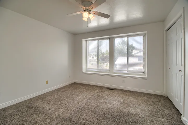 Ceiling fan with light fixture, carpeted flooring, large window with blinds, and white bi-fold closet doors