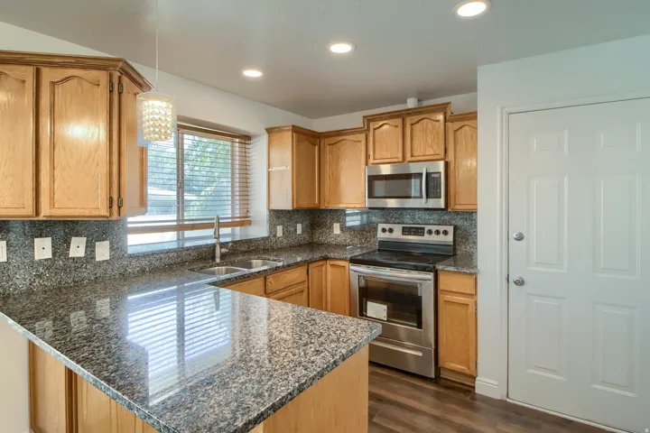 Kitchen featuring granite countertops, wood cabinetry, stainless steel appliances, and wood-finish flooring