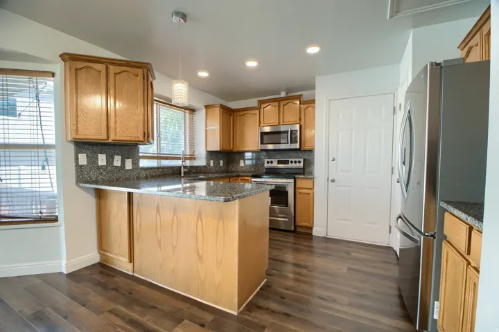 Kitchen featuring wood-finish flooring, light wood cabinetry, granite countertops, stainless steel appliances, and recessed lighting