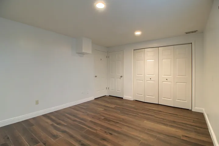 Spacious bedroom with rich wood-finish flooring, recessed ceiling lighting, and dual closets with six-panel doors