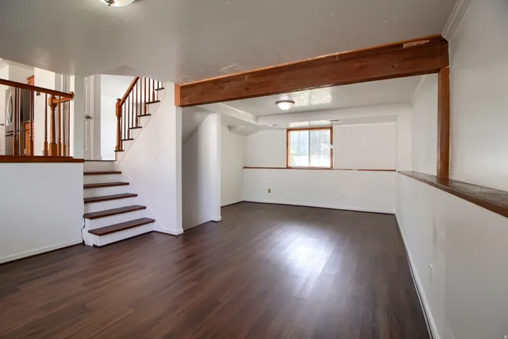 Lower level space featuring wood-finish flooring, a prominent exposed beam, and a window with wood trim