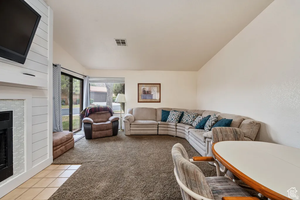 Carpeted living room featuring a fireplace, vaulted ceiling, and sliding doors to patio