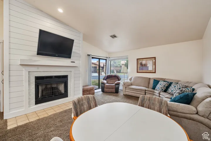 Carpeted living room with vaulted ceiling, recessed lighting, fireplace, and sliding doors to patio