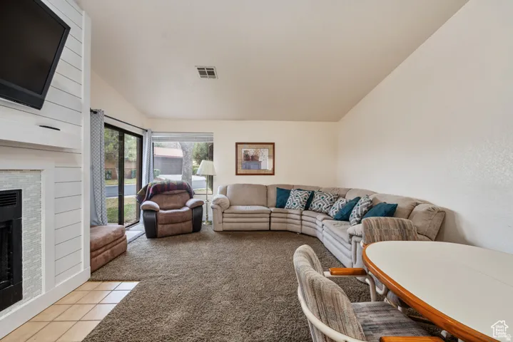 Carpeted living room featuring a fireplace, vaulted ceiling, and sliding doors to patio
