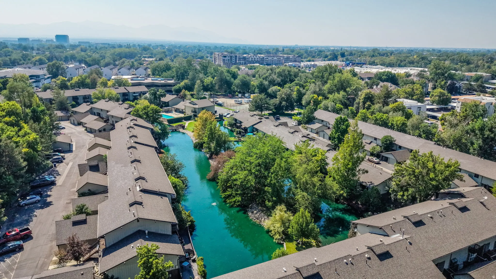 Community with multiple buildings, a central water feature, mature trees, and a swimming pool