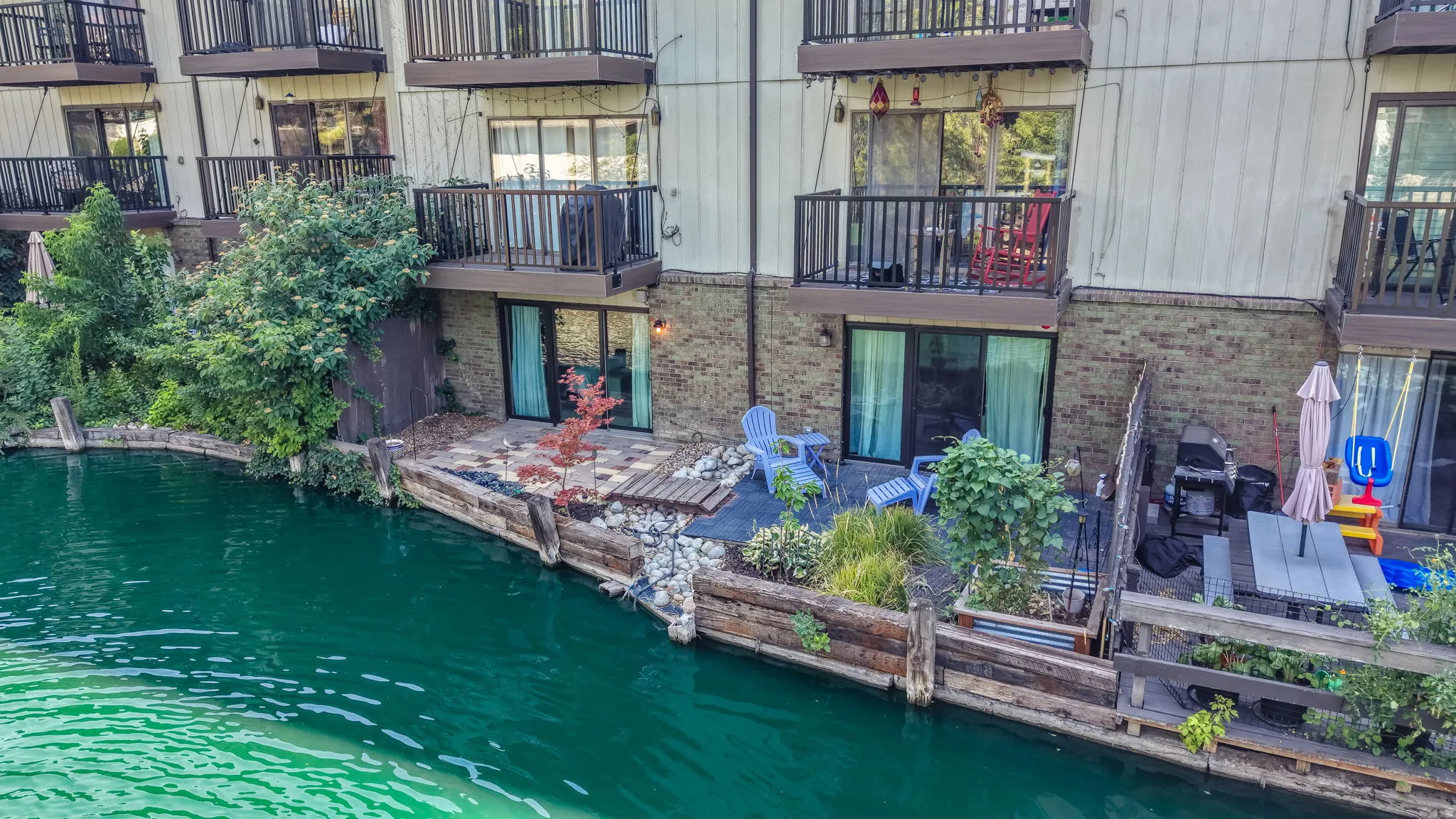 Private ground-level patio with sliding glass doors, water frontage, and wood retaining wall