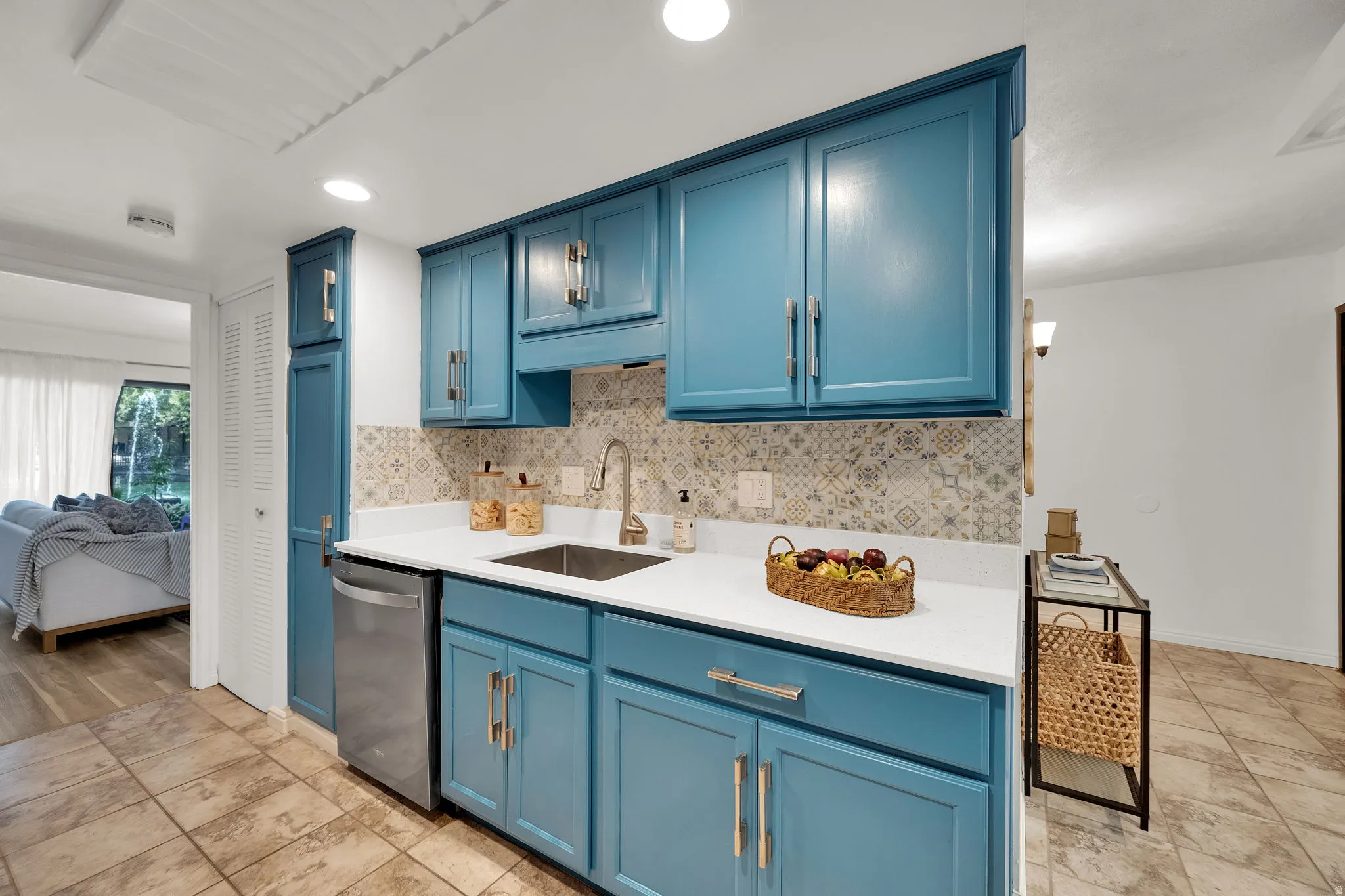 Turquoise cabinetry with brushed nickel hardware, white countertops, stainless steel sink, patterned tile backsplash, and tile flooring