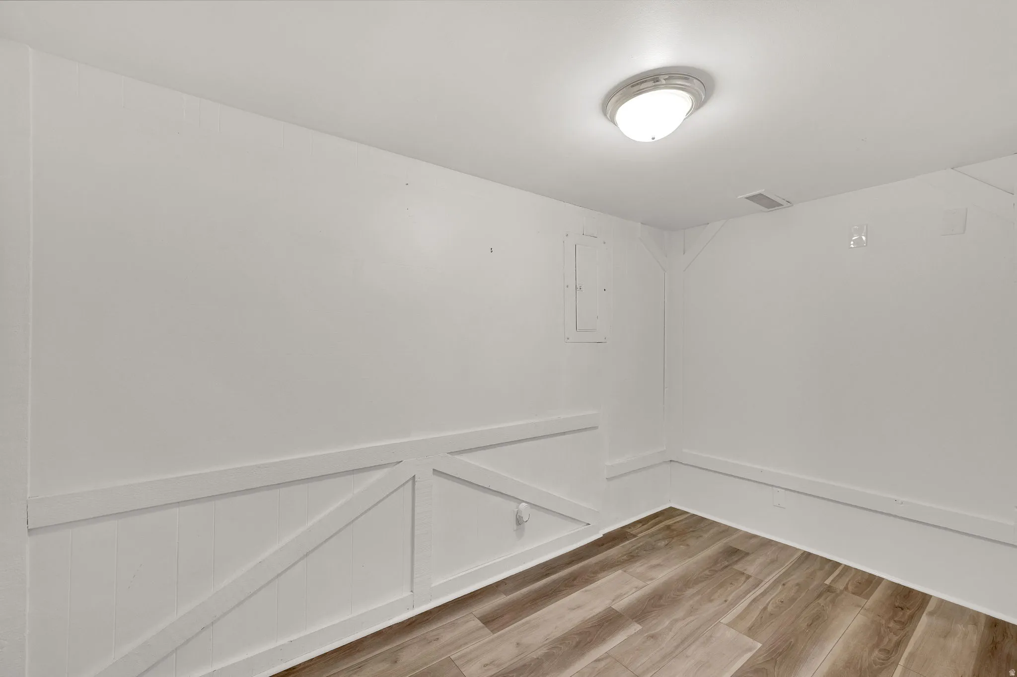 Wood-finish flooring, white walls, and a flush-mount ceiling light
