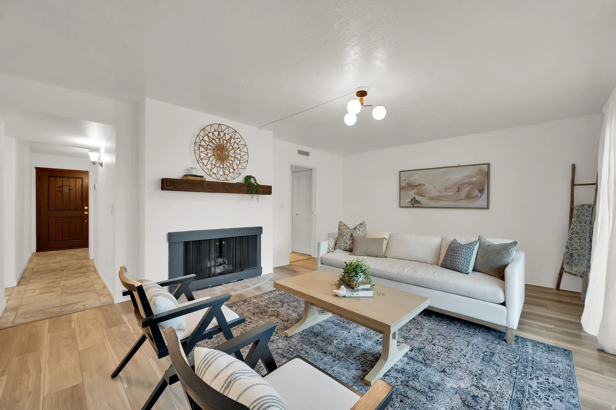 Living area featuring wood-finish flooring, a fireplace with a dark mantel, a wood-beam floating shelf, and a modern ceiling light fixture