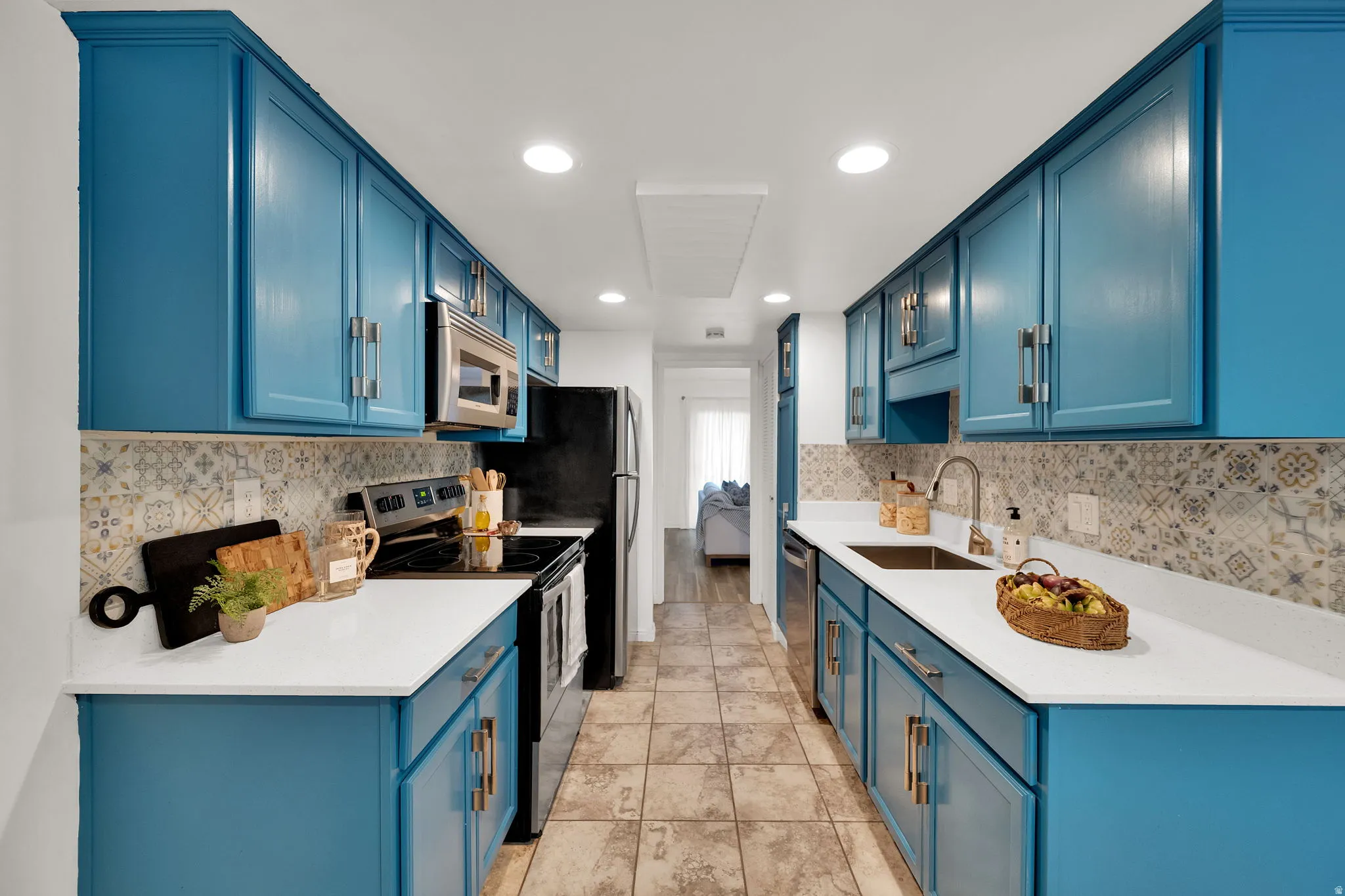 Kitchen featuring blue cabinetry, white countertops, stainless steel appliances, patterned tile backsplash, and tile flooring