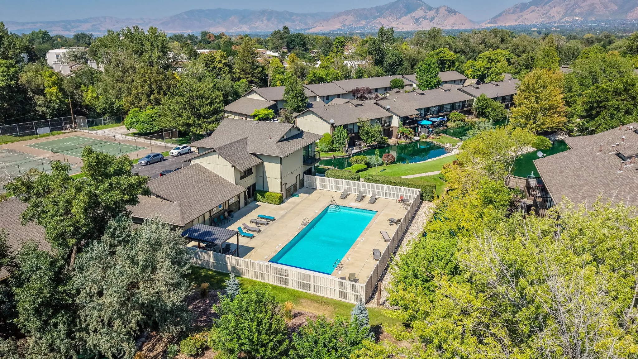 Outdoor swimming pool, fenced pool deck, expansive green spaces, surrounding trees, distant mountains
