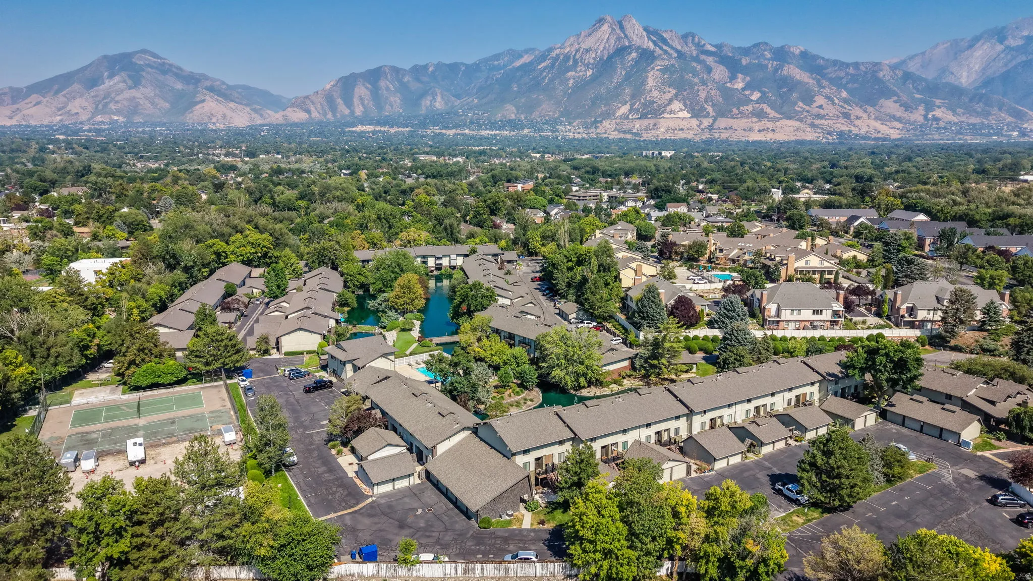Expansive property featuring multiple residential buildings, a tranquil pond, a swimming pool, and tennis courts, all set against a prominent mountain backdrop