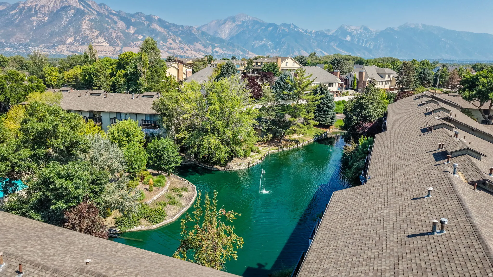Expansive community grounds featuring a central pond with fountain, mature landscaping, and mountain backdrop