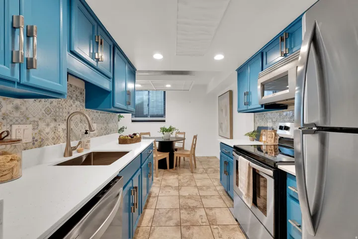 Galley kitchen featuring blue cabinetry, stainless steel appliances, patterned tile backsplash, white countertops, and tile flooring