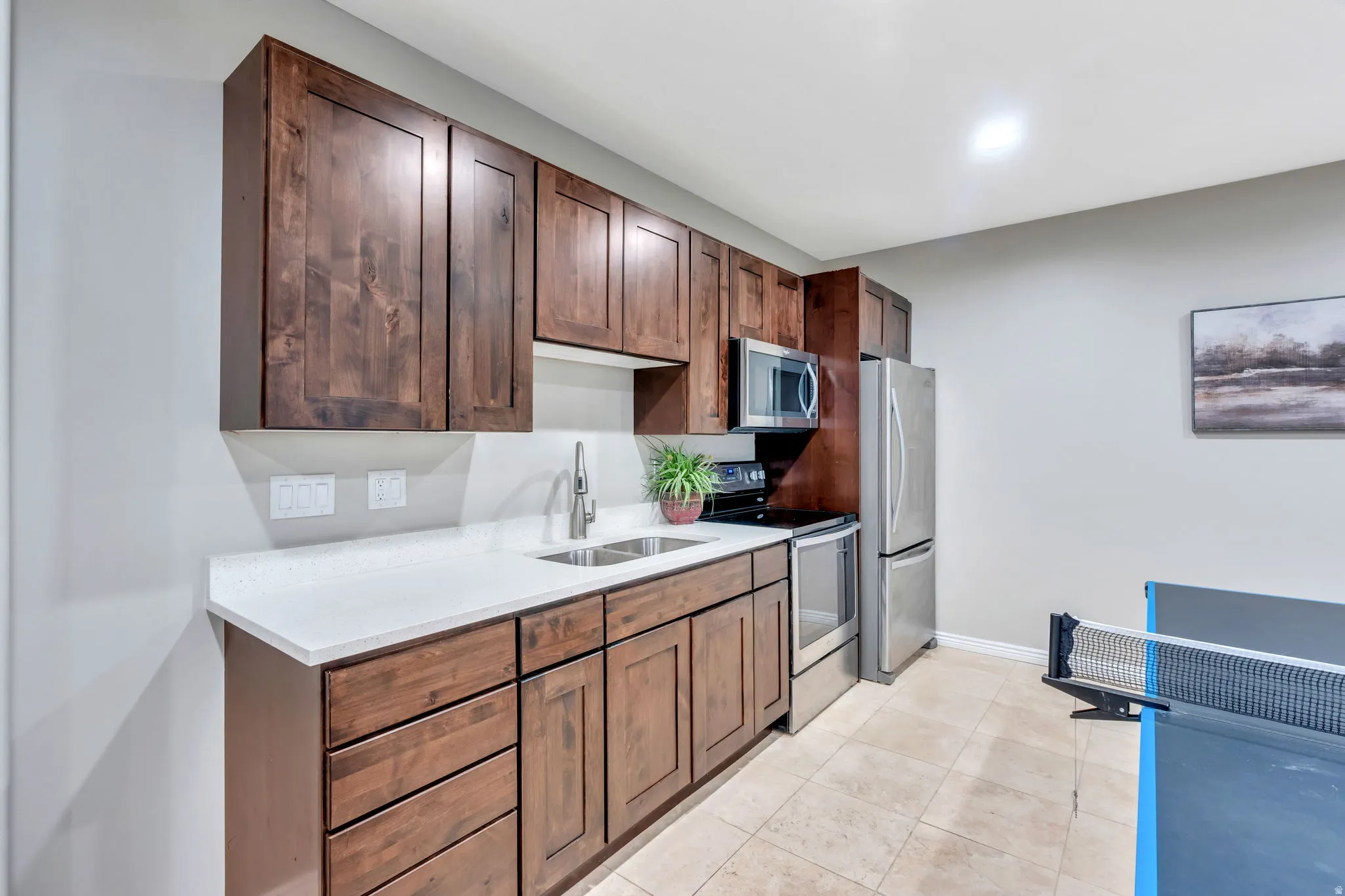 Compact kitchen featuring wood cabinetry, white countertops, stainless steel appliances, and a double basin sink with a gooseneck faucet