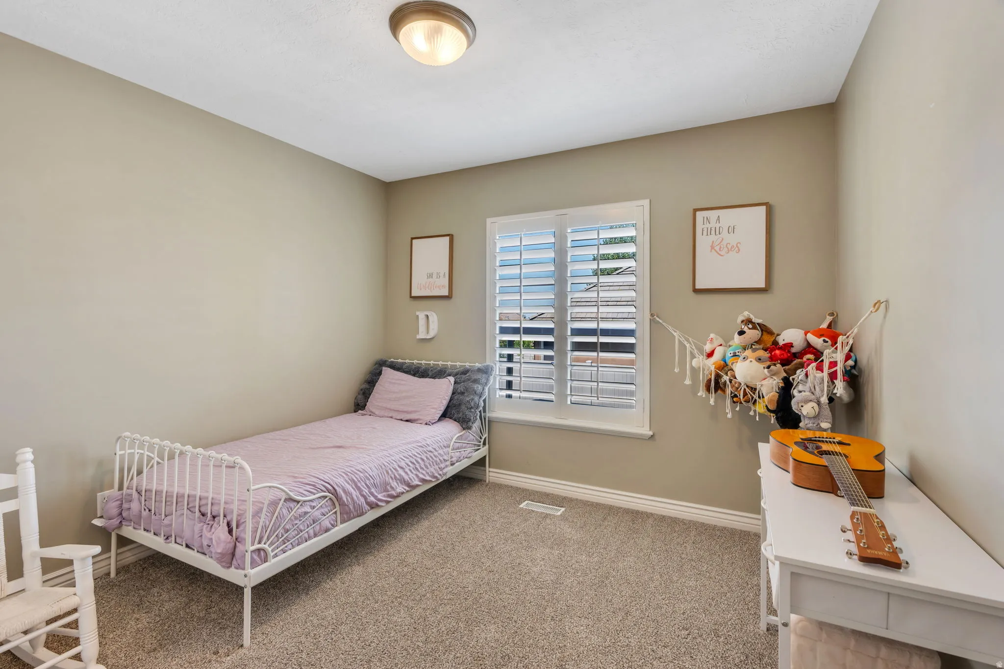 Interior room featuring neutral wall paint, textured carpeting, and a window with white plantation shutters