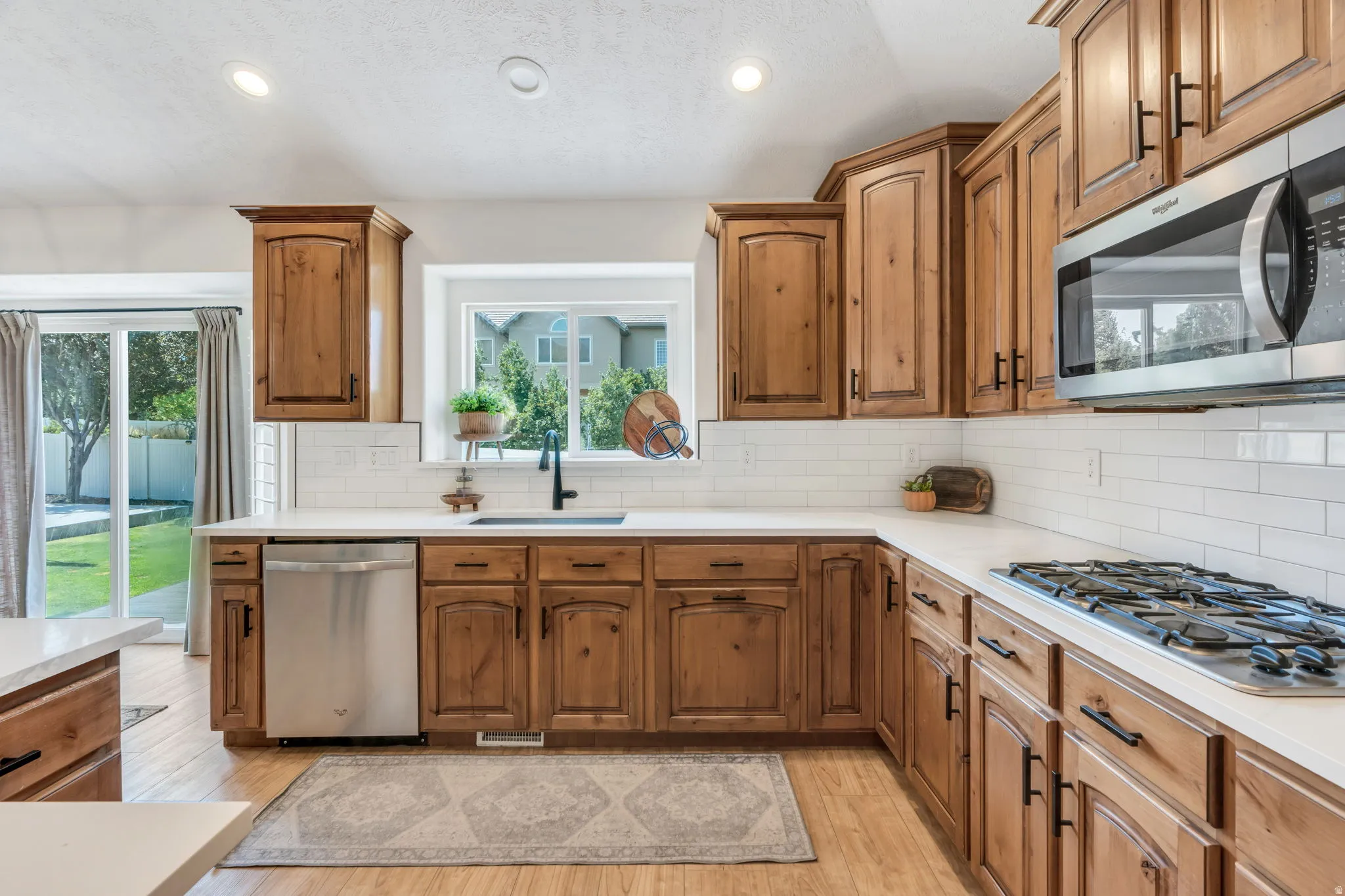 Kitchen featuring wood cabinetry, white countertops, stainless steel appliances, a subway tile backsplash, and wood-finish flooring
