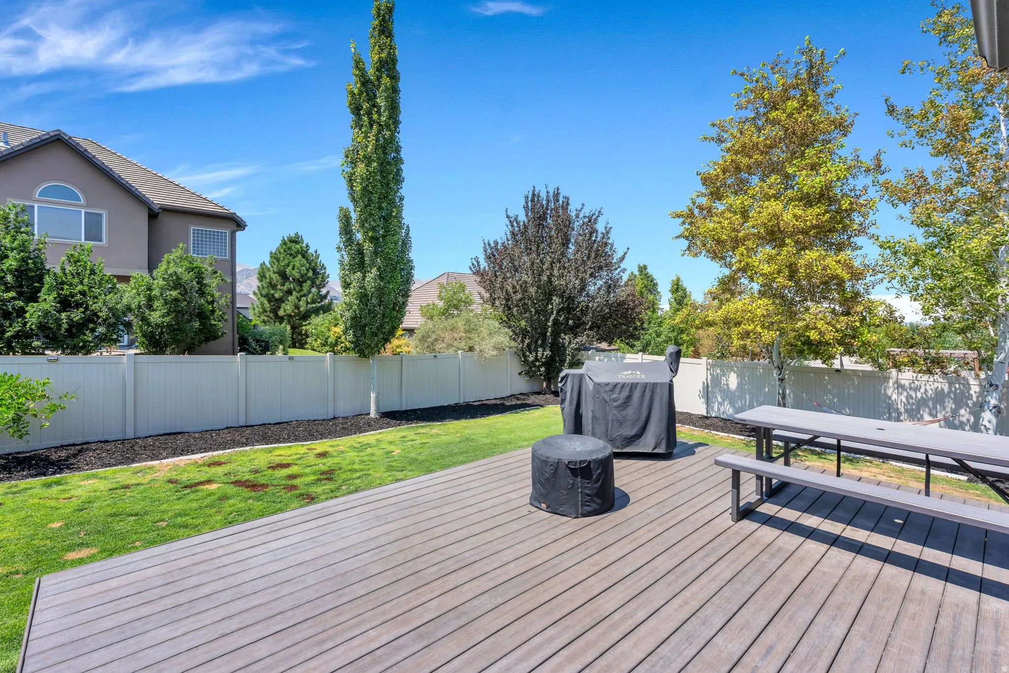 Spacious backyard featuring a substantial wood-finish deck, verdant lawn, and mature trees