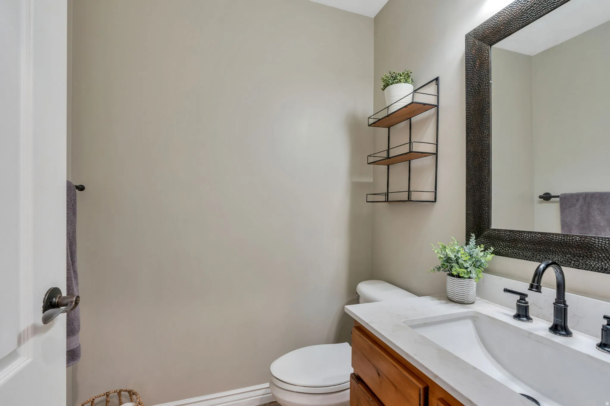 Powder room featuring a wood-finish vanity with a white countertop and integrated sink, matte black faucet, and a large decorative framed mirror