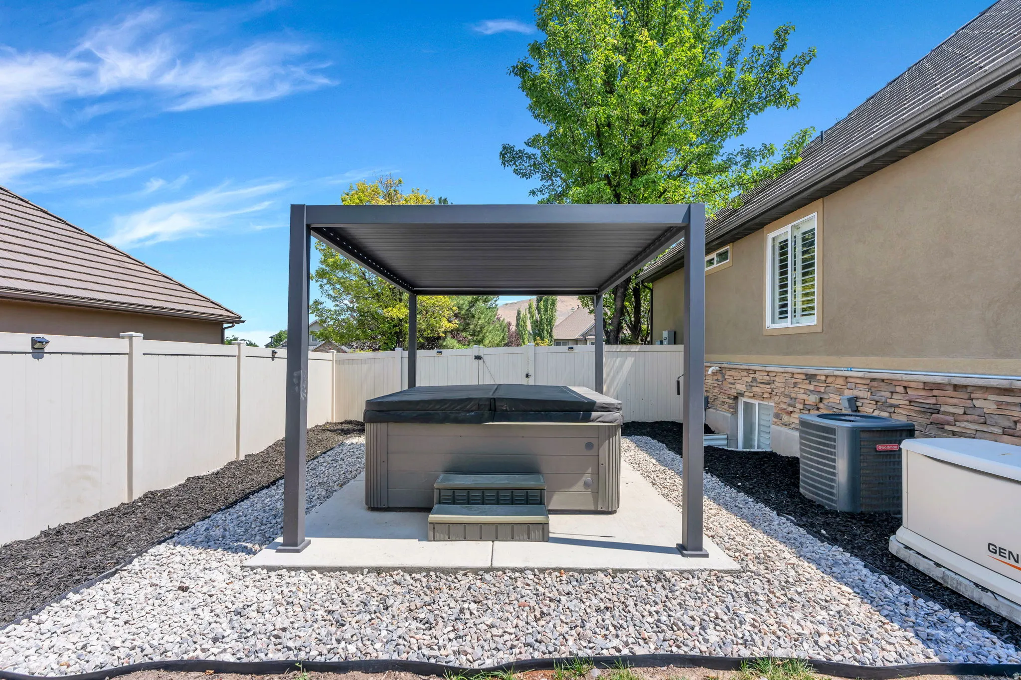 Outdoor spa area featuring a modern pergola, white vinyl fencing, and decorative gravel landscaping