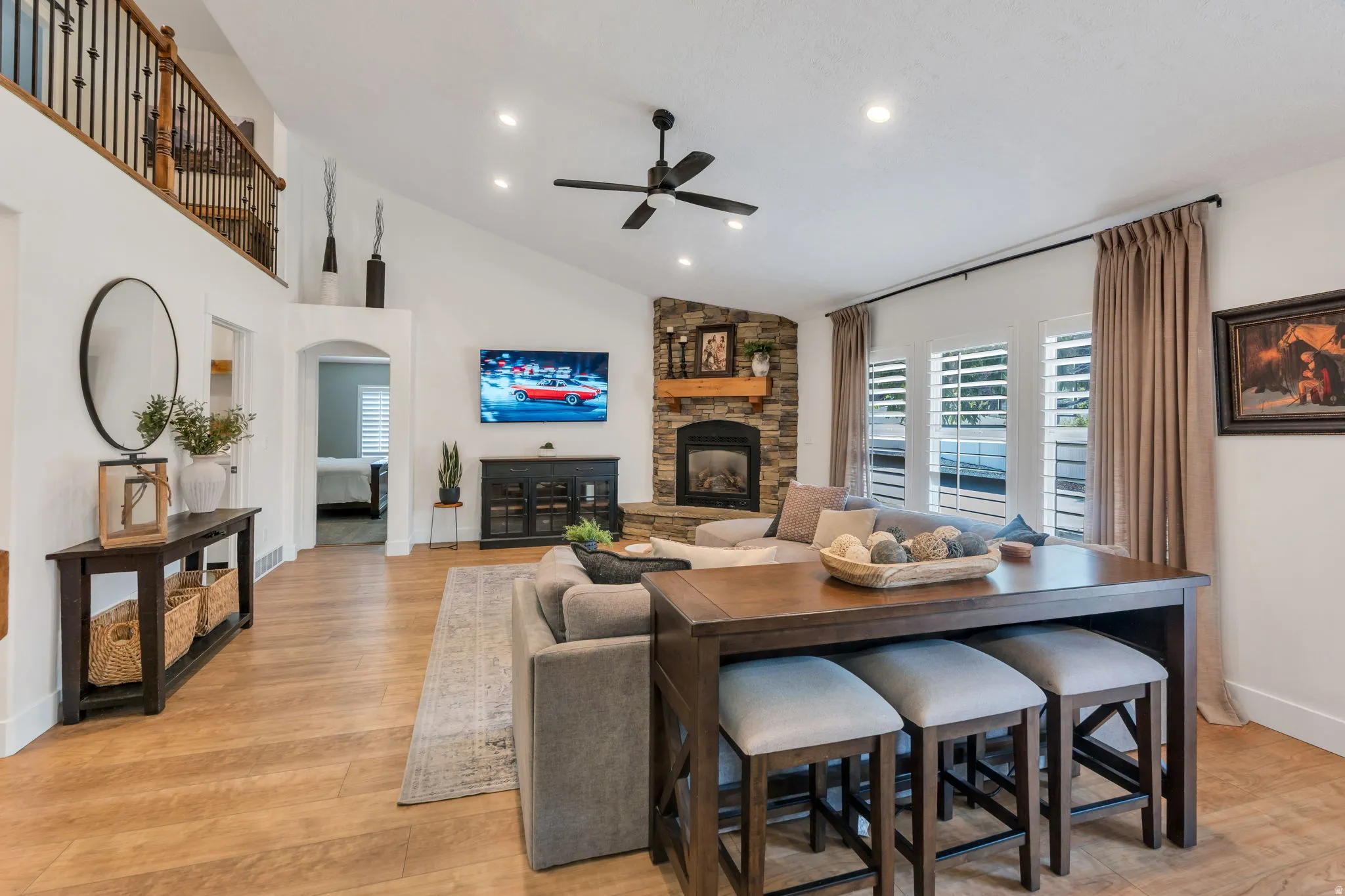 Spacious living area featuring a vaulted ceiling with recessed lighting and a ceiling fan, wood-finish flooring, and a corner stone-front fireplace with a wood mantel