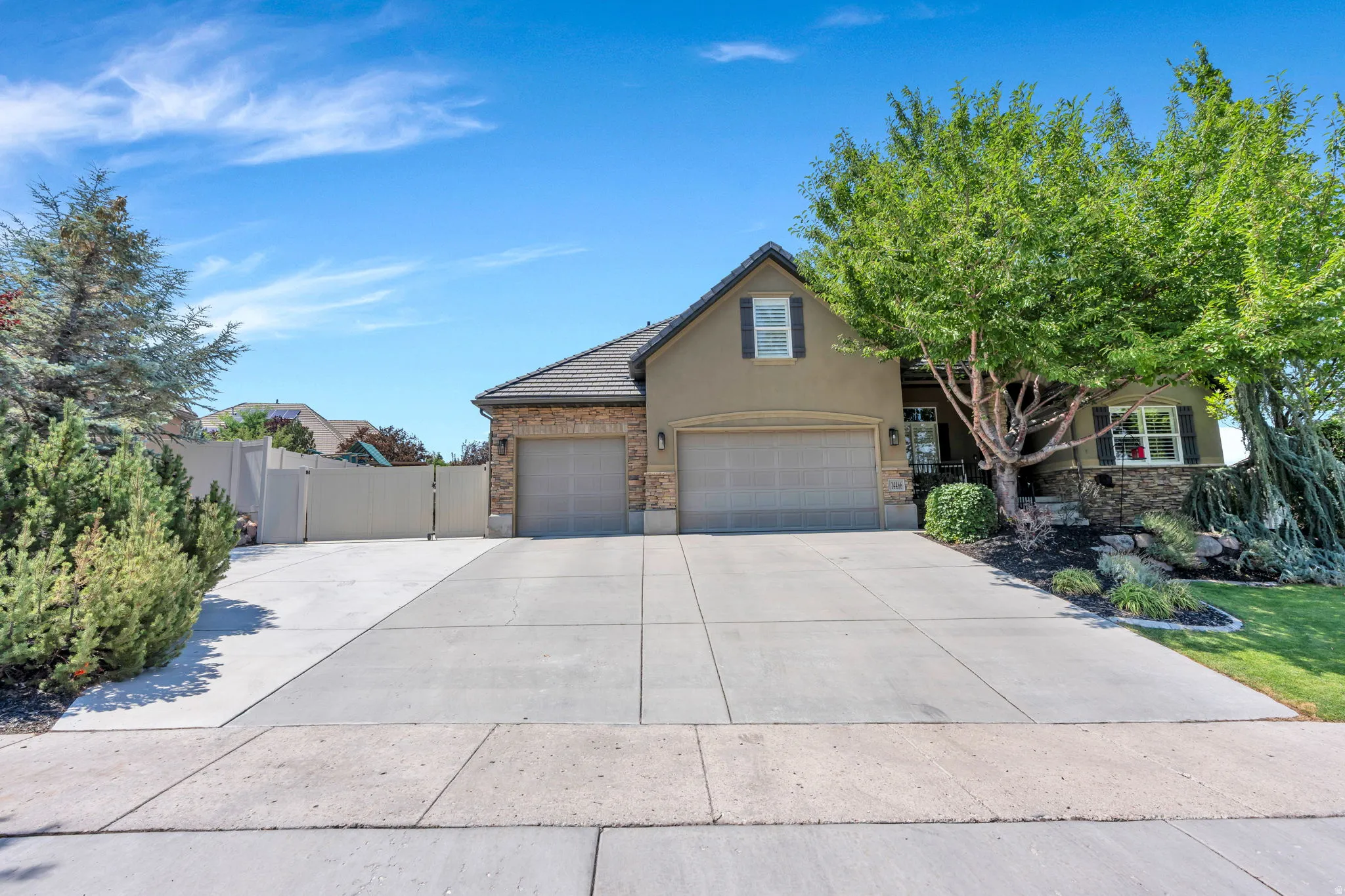 Stucco and stone facade home featuring a multi-car driveway, two-car garage, and mature landscaping