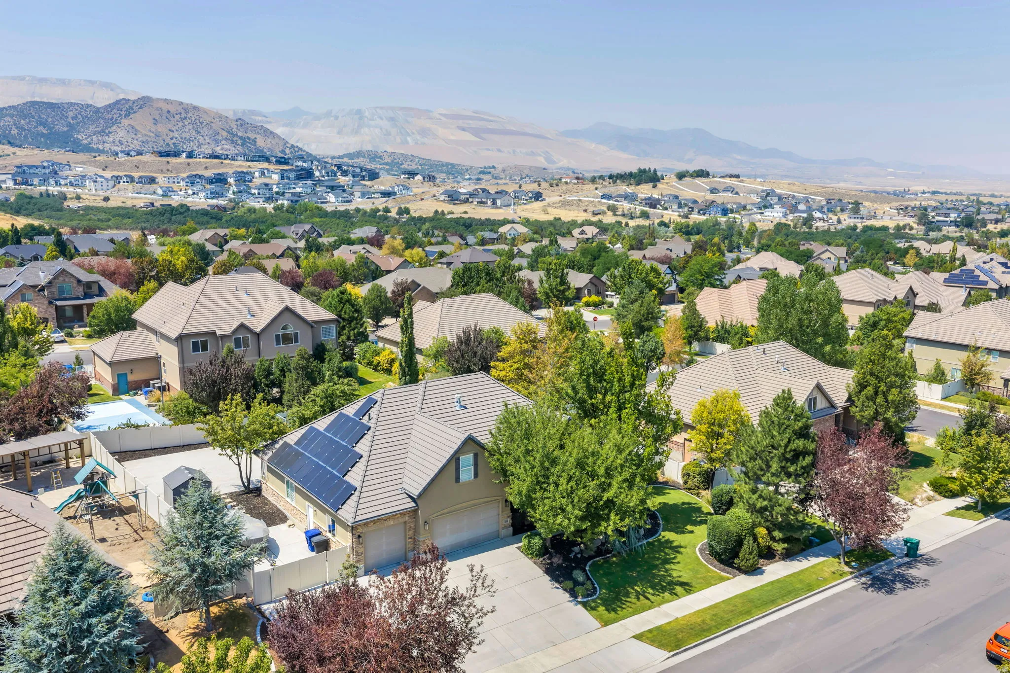 Stunning aerial view showcasing this residence featuring a solar panel array on the roof, mature landscaping with established trees throughout the grounds, a curved driveway with professional hardscaping, a resort-style backyard with in-ground pool and sp