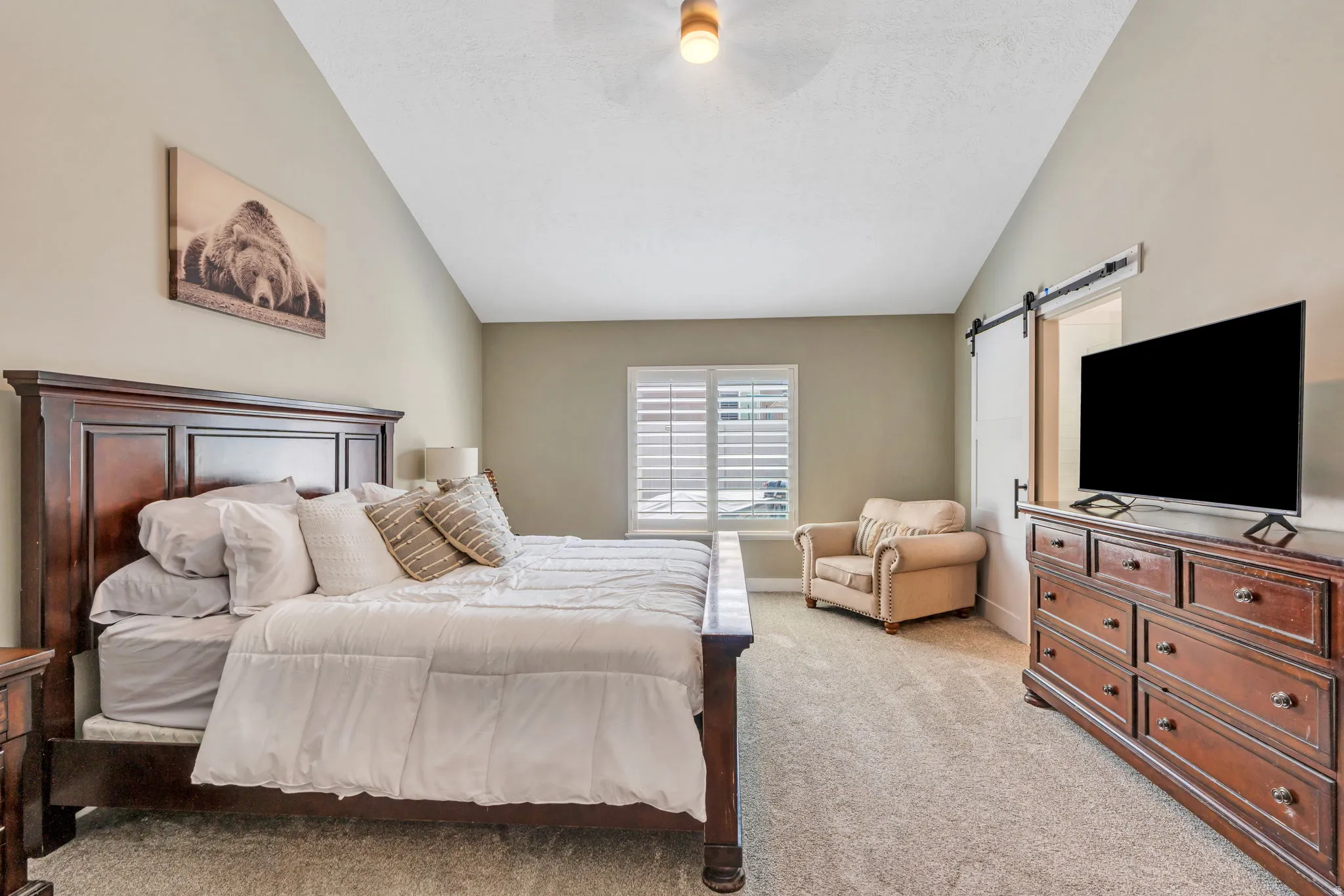 Spacious room featuring vaulted ceilings, light-toned carpeting, and a window with plantation shutters