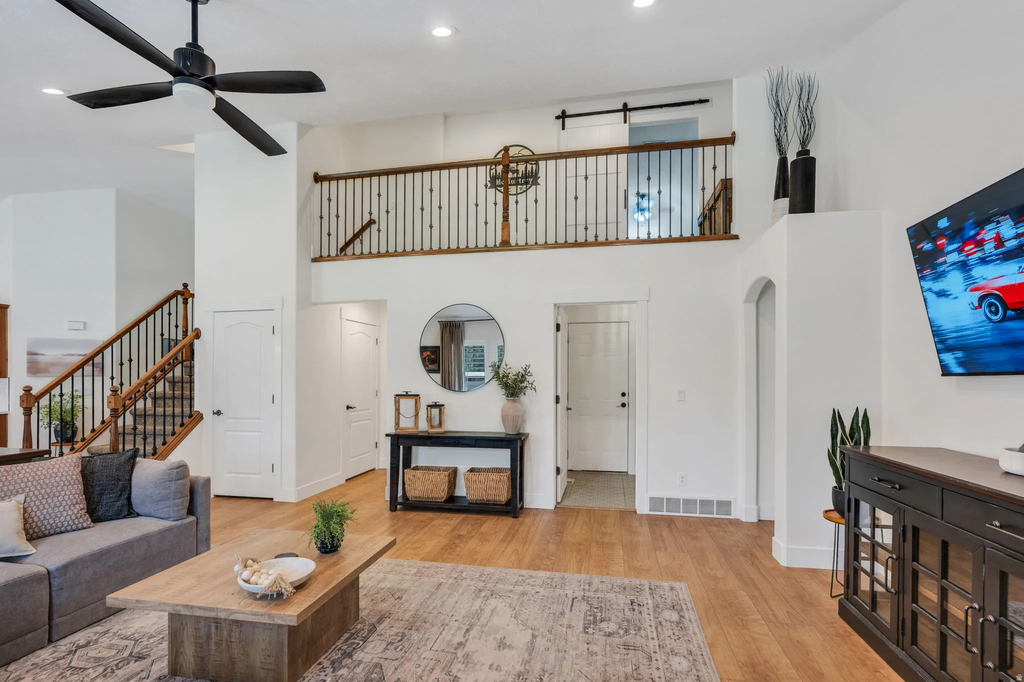 Spacious living area featuring high ceilings, wood-finish flooring, and a prominent staircase with dark iron balusters