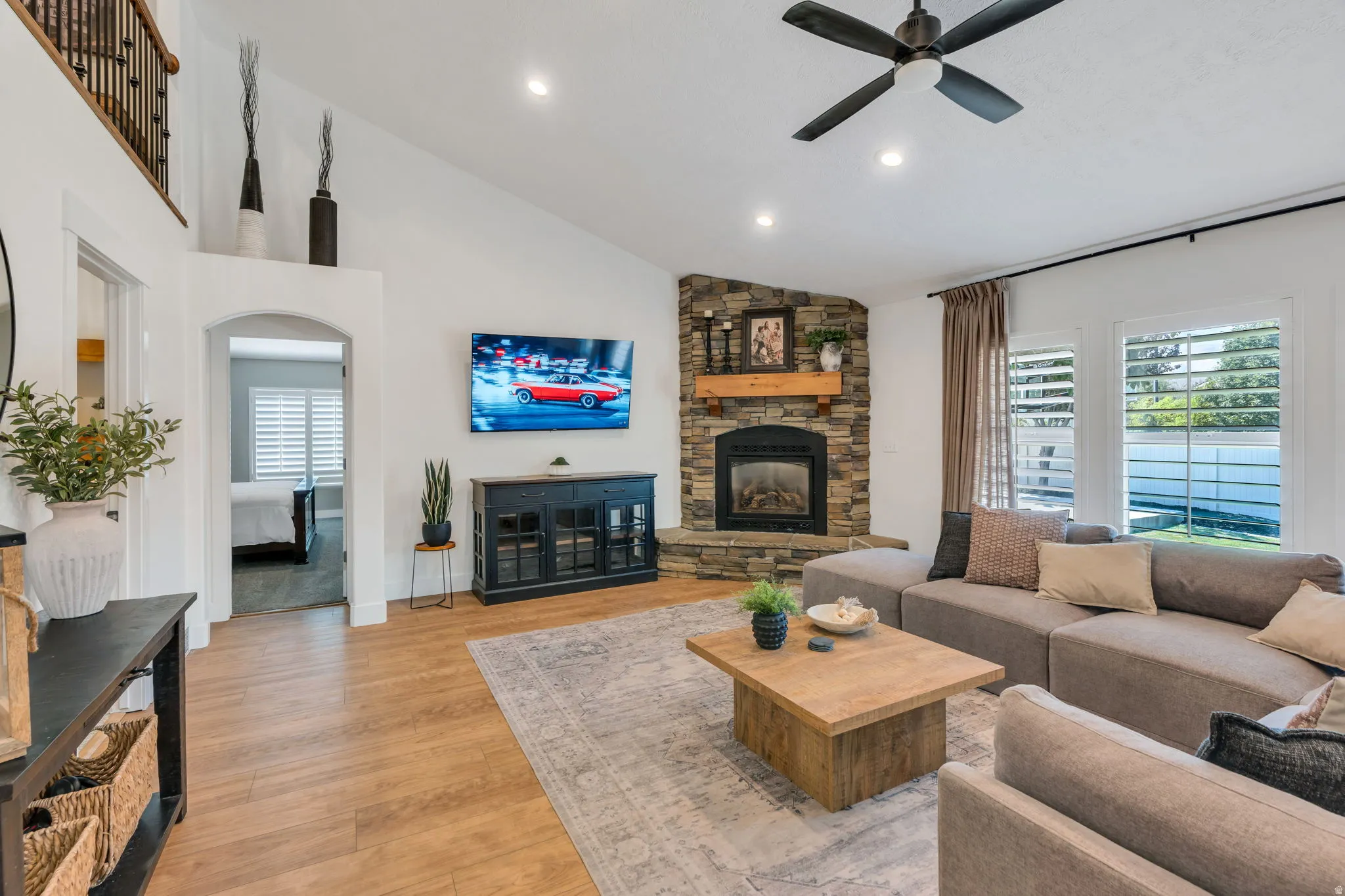 Living area featuring a stone-clad fireplace with a wood mantel, vaulted ceilings, recessed lighting, wood-finish flooring, and a ceiling fan