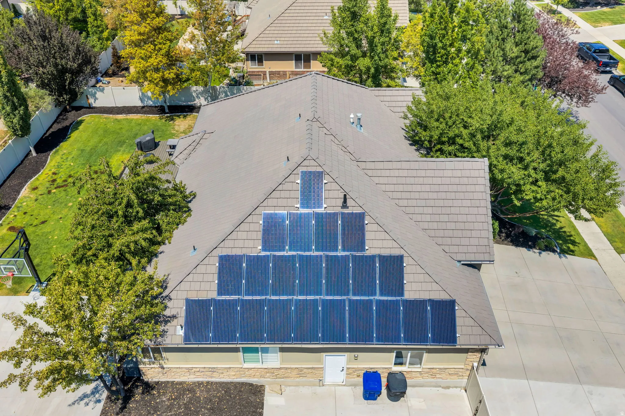 Property featuring a shingle roof with extensive solar panel installation, a stone facade, and a concrete driveway