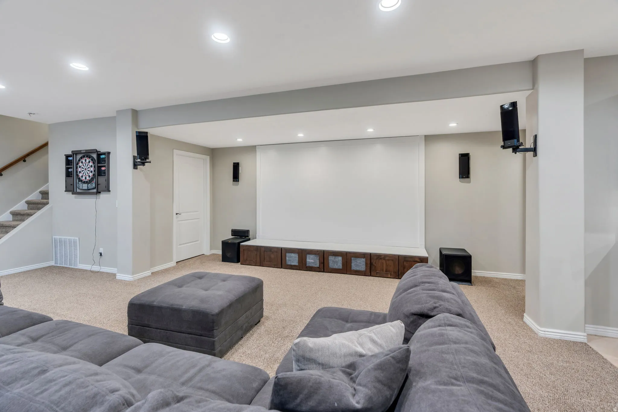 Finished lower level featuring a large projection screen, recessed lighting, carpeted flooring, and a built-in storage console