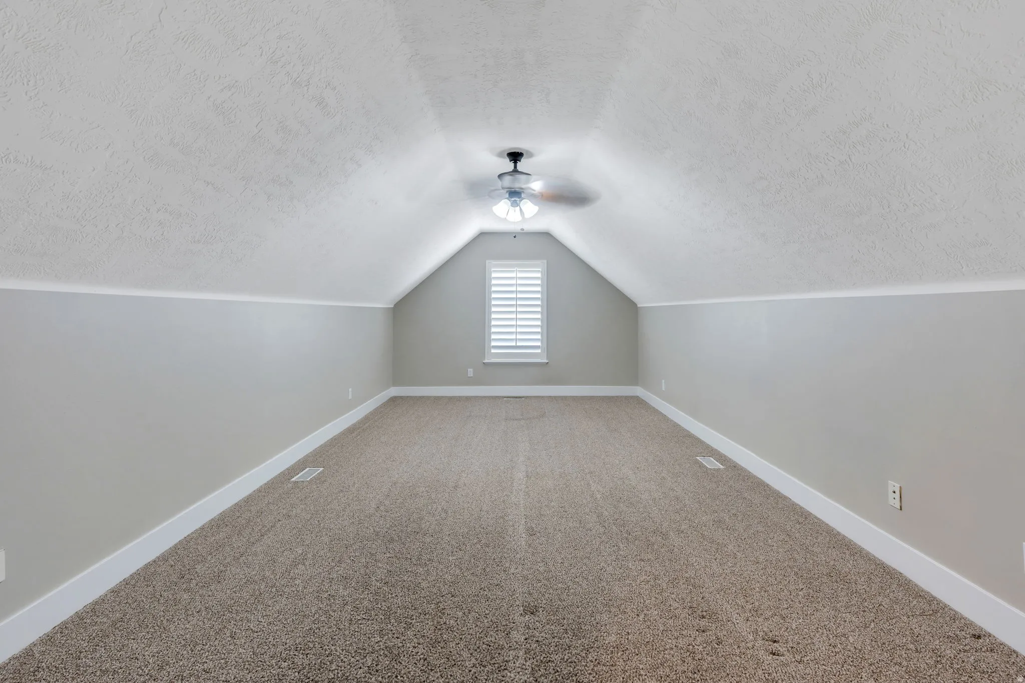 Carpeted loft space featuring sloped ceilings, a ceiling fan with light fixture, a window with louvered shutters, and baseboard trim