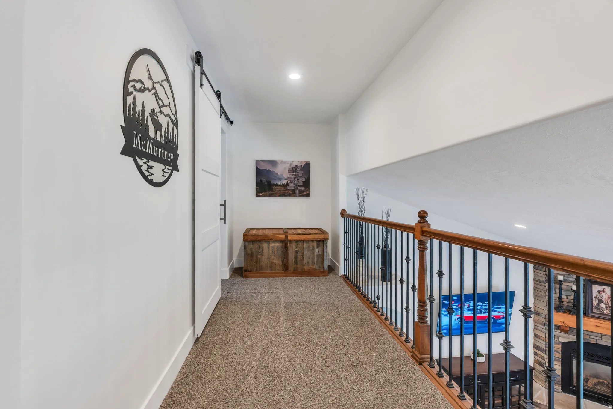 Upper-level hallway featuring a sliding barn door with black hardware, recessed lighting, and light-toned carpet flooring