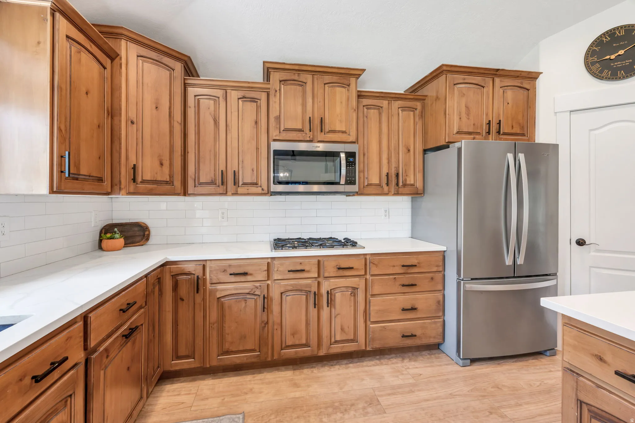 Kitchen featuring wood cabinetry with dark hardware, white countertops, white subway tile backsplash, stainless steel appliances, and wood-finish flooring