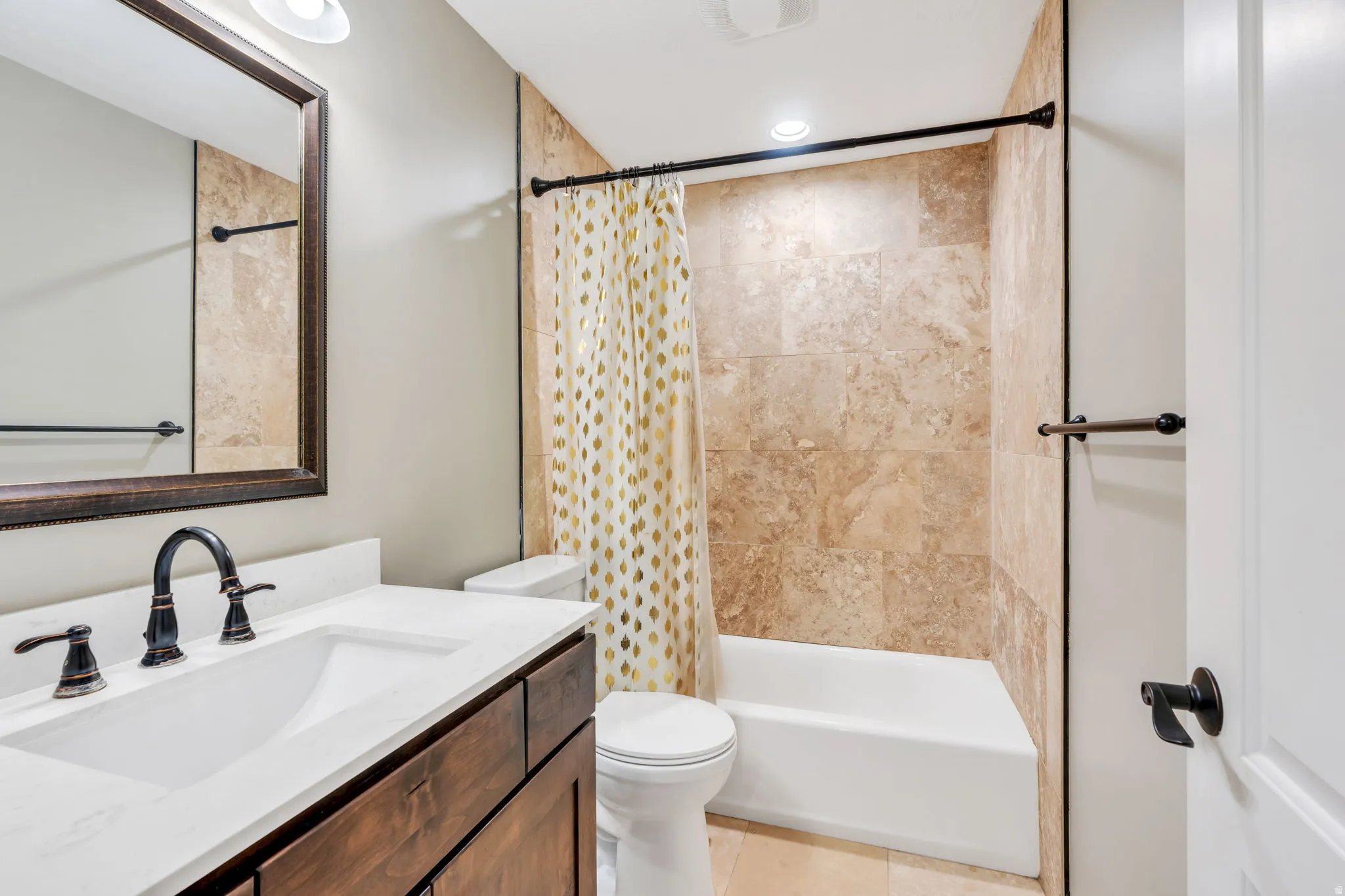Bathroom featuring a vanity with an integrated sink and bronze-finish faucet, a framed mirror, a tiled shower/tub combination, recessed lighting, and a white toilet