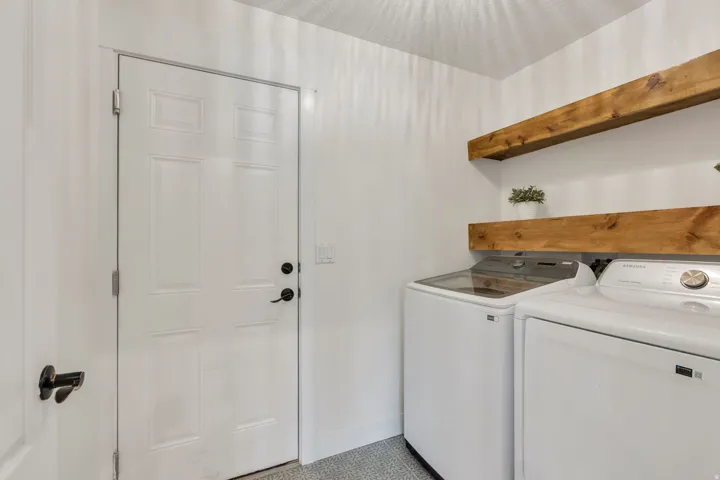 Dedicated laundry area featuring a paneled door with matte black hardware, wood-finish floating shelves, and patterned tile flooring