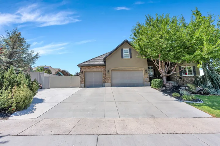 Stucco and stone facade home featuring a multi-car driveway, two-car garage, and mature landscaping