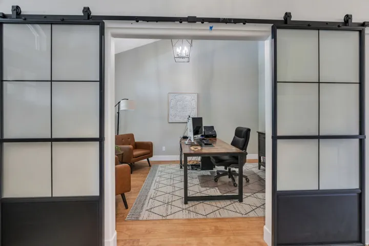 Dual black framed sliding barn doors with frosted glass panels open to a room featuring wood-finish flooring, light gray walls, and a contemporary chandelier