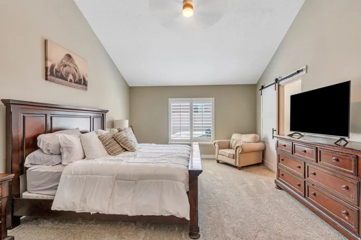 Spacious room featuring vaulted ceilings, light-toned carpeting, and a window with plantation shutters